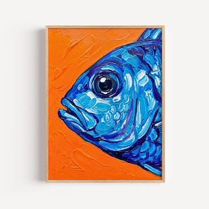 以下が含まれることがあります： 厚みのあるテクスチャーのインパスト技法で描かれた青い魚の長方形の額入り絵画。魚は横向きで、鮮やかなオレンジ色の背景に描かれています。作品は明るい色調の木製フレームに収められています。