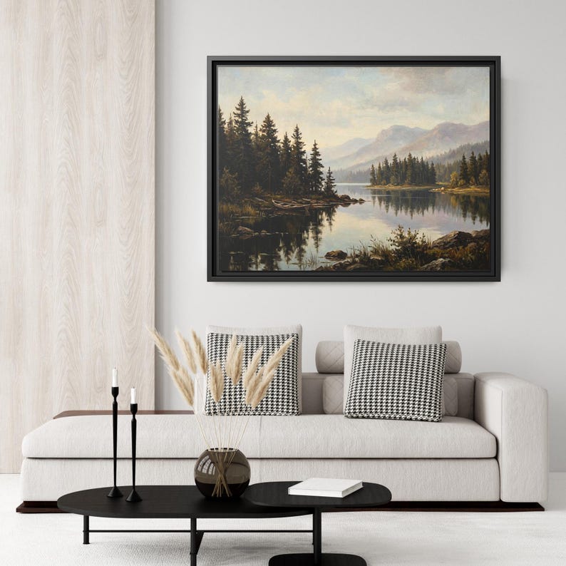 May include: A framed landscape painting depicting a serene lake surrounded by dense evergreen forests and distant mountains under a soft, cloudy sky. The artwork features deep green, brown, and muted blue tones, reflecting the trees in the water.
