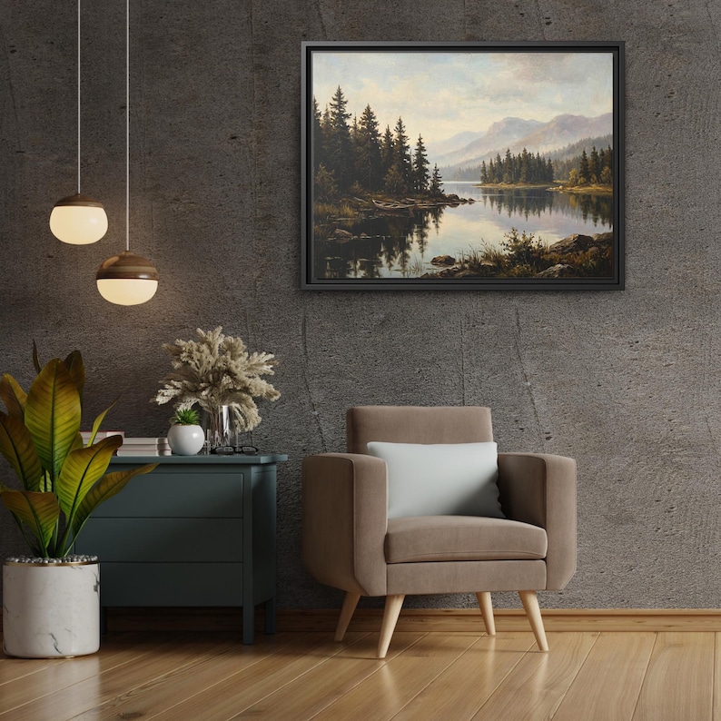 May include: A framed landscape painting depicting a calm lake surrounded by dense evergreen trees and distant mountains under a soft, cloudy sky. The artwork features muted earth tones, deep greens, and reflective water, presented in a black frame.