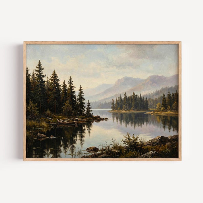 May include: A landscape painting in a light wood frame depicting a calm lake surrounded by dense evergreen forests and distant mountains under a soft, cloudy sky. A small wooden rowboat rests near the rocky shoreline in the foreground.