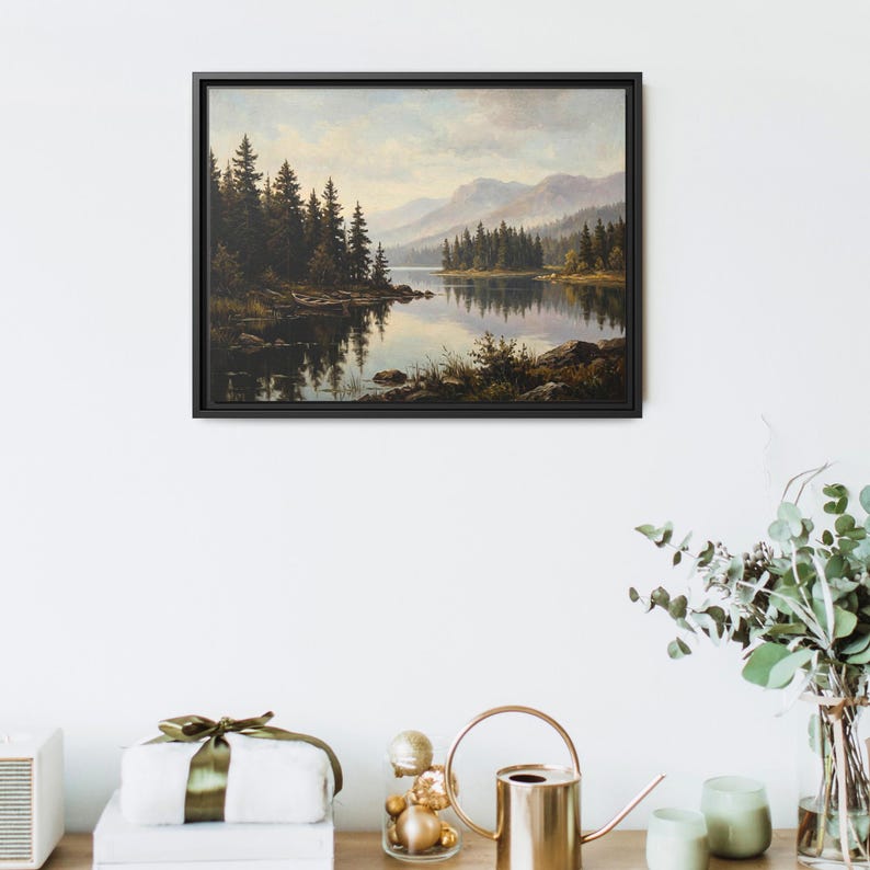 May include: A framed landscape painting depicting a calm lake surrounded by dense evergreen forests and distant mountains under a soft, cloudy sky. The artwork features deep green, brown, and muted blue tones, capturing a serene natural scene.