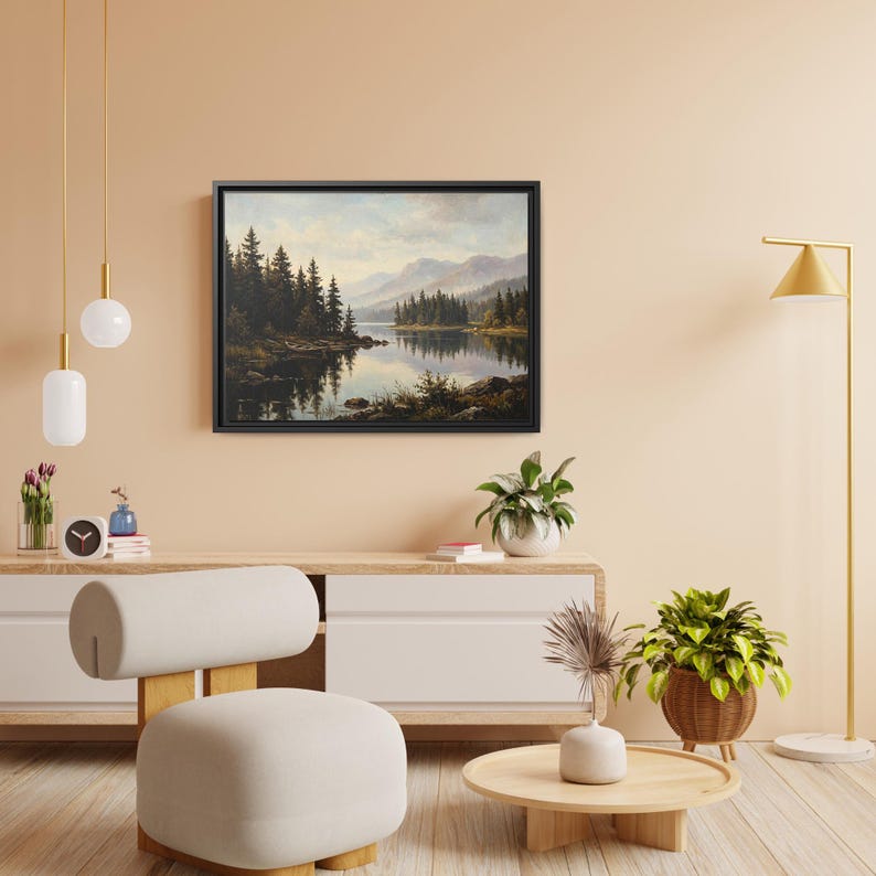 May include: A rectangular landscape painting in a black frame depicting a calm lake surrounded by dense evergreen pine trees and distant mountains under a soft, cloudy sky, with the reflection of the trees visible on the water surface.