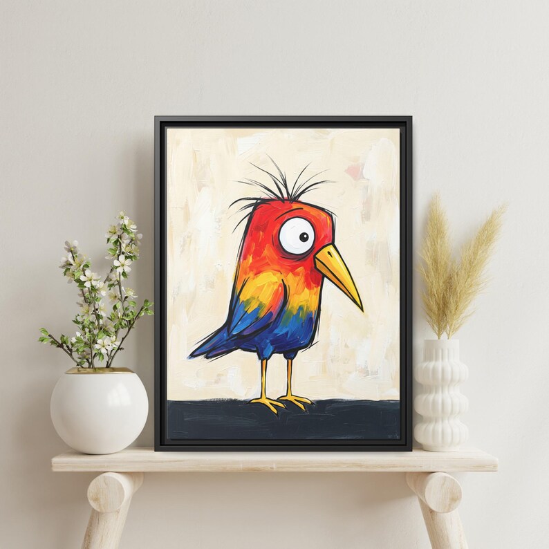 May include: A framed wall art print featuring a stylized illustration of a bird with a bright red, orange, and blue body, a yellow beak, and large white eyes with black pupils, set against a light beige background with a dark base.