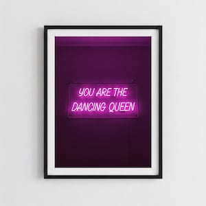 Könnte beinhalten: Ein gerahmter Druck mit einem Neon-Schild mit den Worten "YOU ARE THE DANCING QUEEN" in leuchtendem Pink vor einem dunkelvioletten Hintergrund. Das Schild ist rechteckig und hängt mittig im schwarzen Rahmen.