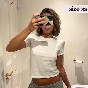 May include: A plain white short-sleeved t-shirt with a crew neckline. The garment is labeled as size xs. The shirt features a simple, solid-colored design with a standard fit, constructed from a lightweight fabric suitable for casual wear.