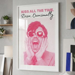 May include: A framed pink and white print with the text "KISS ALL THE TIME. Disco, Occasionally." The image features a person wearing sunglasses and a pink suit, with their hands on their face and mouth open.