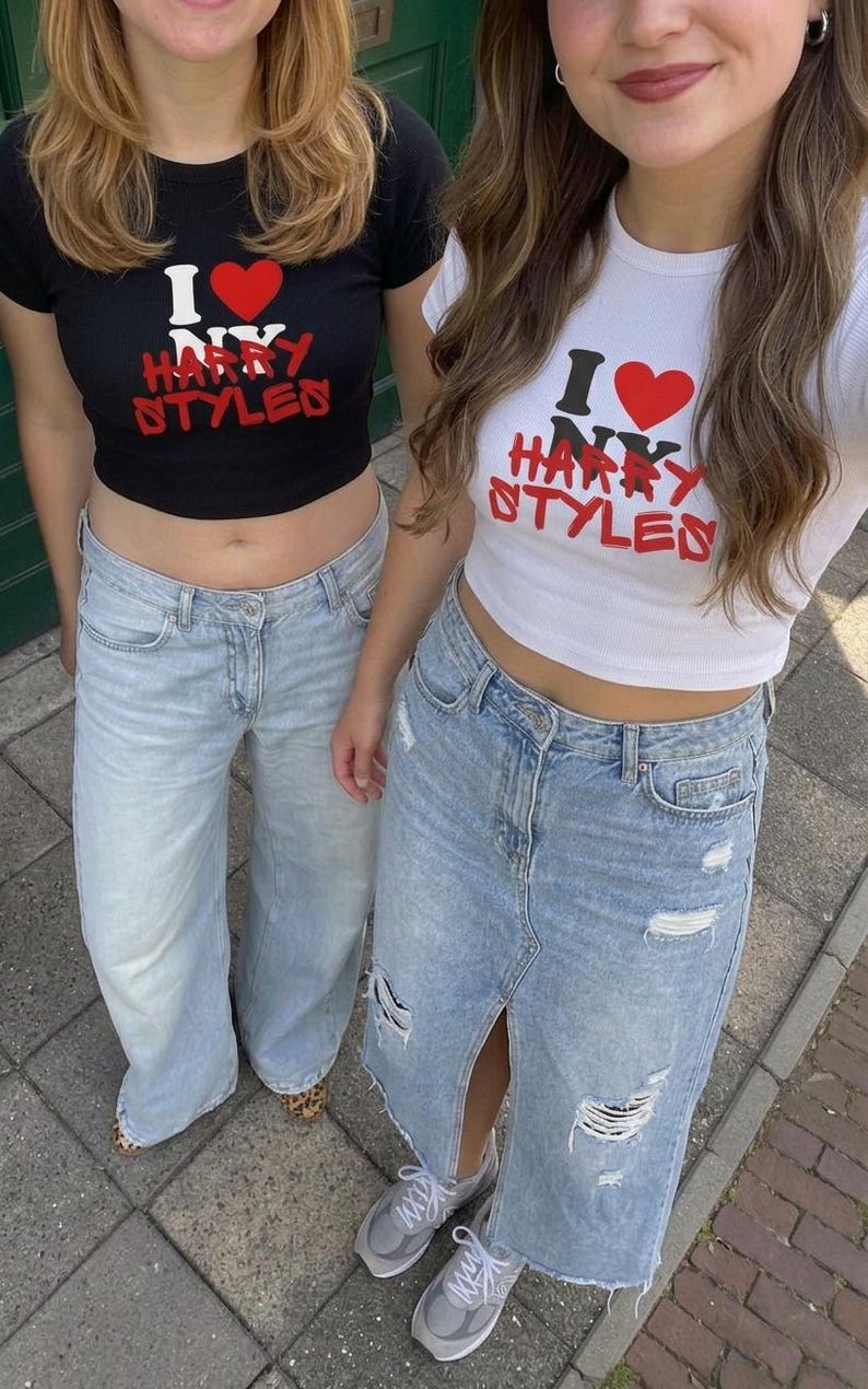 May include: Two cropped t-shirts, one black and one white, each featuring a red heart icon and the text I LOVE NY HARRY STYLES in red and black lettering. The black shirt is paired with light blue jeans, and the white shirt with a distressed denim skirt.
