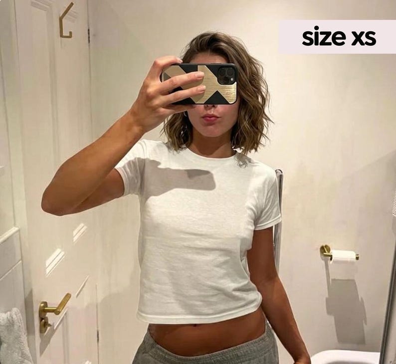 May include: A plain white short-sleeved t-shirt with a crew neckline. The garment is labeled as size xs. The shirt features a simple, solid-colored design with a standard fit, constructed from a lightweight fabric suitable for casual wear.