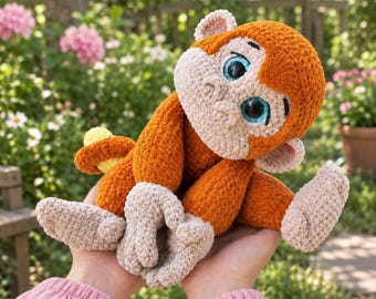 May include: A plush monkey toy crafted from soft, textured yarn in shades of burnt orange and cream. The monkey features large, glossy blue eyes, rounded ears, and a curled tail. The stuffed animal has a light cream face, hands, and feet.