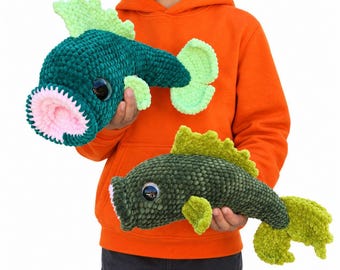 May include: Two plush fish toys made of soft, textured yarn. The larger fish is dark green with a light green fin and tail, featuring a wide, open mouth with pink lining. The smaller fish is olive green with lime green fins and a white-lined mouth.