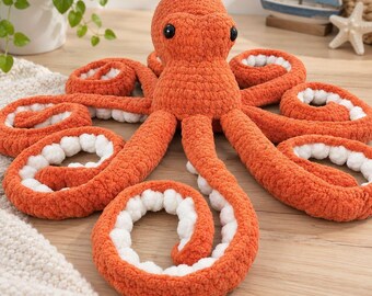 May include: A plush octopus toy crafted from orange yarn with a textured, crocheted surface. The octopus features a rounded head, two black plastic eyes, and eight long, curled tentacles. The underside of each tentacle is lined with white yarn.