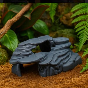 May include: A grey reptile hide resembling a rock formation, featuring a step ledge and cave opening. This reptile habitat is designed to offer shelter and enrichment for reptiles, amphibians, and invertebrates.
