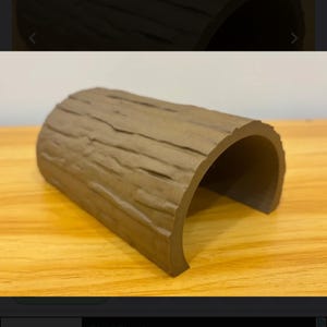 May include: A brown, wood-textured reptile hide shaped like a log. The hide has a curved opening and is approximately 38 cm long, 28 cm wide, and 18 cm high. The product is designed for reptile habitats.