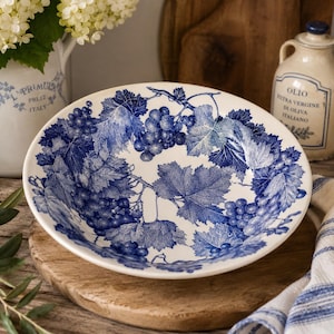 May include: A round ceramic bowl featuring a detailed blue and white transferware pattern of grape clusters and vine leaves. The interior of the bowl is decorated with a repeating botanical motif of fruit and foliage against a white background.