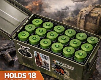 May include: An olive green metal ammo can organizer featuring a black insert that holds 18 green 37mm rounds. The exterior of the container is decorated with various stickers and displays the text 37MM AMMO CAN ORGANIZER and HOLDS 18 ROUNDS!