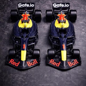 May include: Two identical dark blue and yellow Formula 1 race car models featuring the number 1 on the nose, Red Bull branding on the front wing, and Gate.io text on the rear wing. These miniature vehicles have black tires and aerodynamic bodies.
