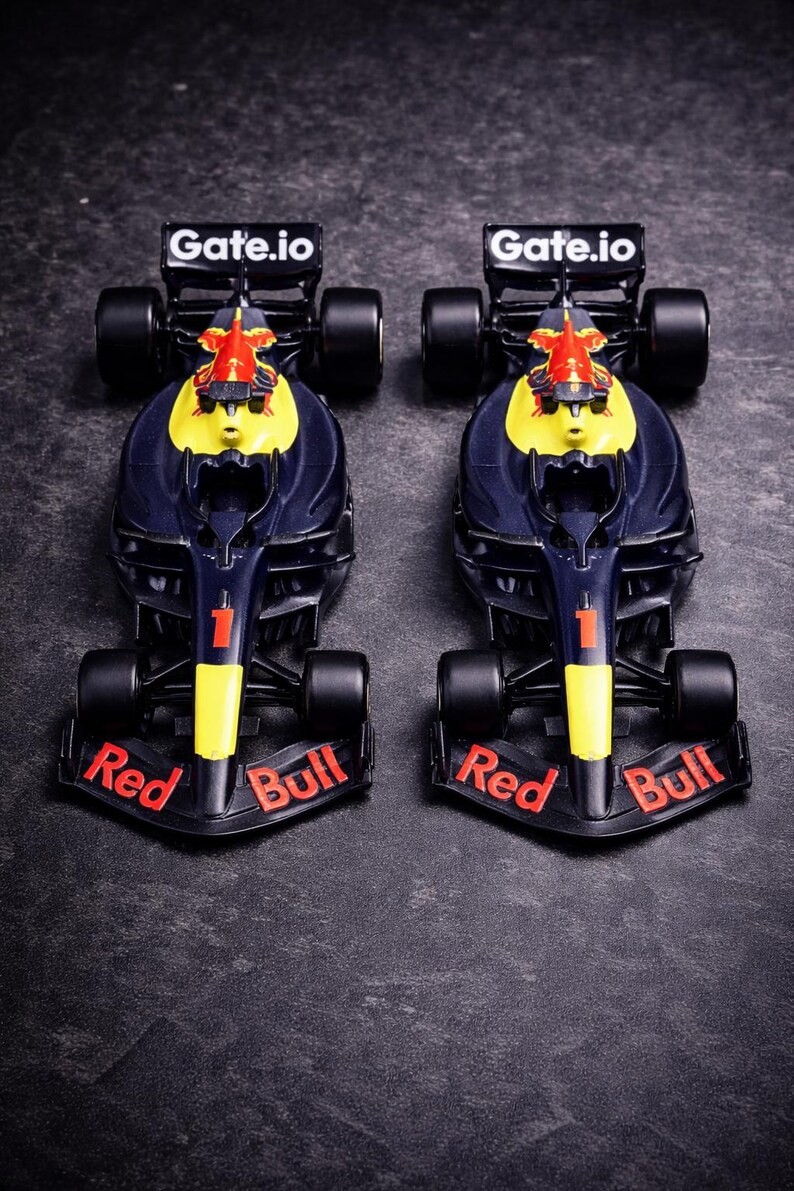 May include: Two identical dark blue and yellow Formula 1 race car models featuring the number 1 on the nose, Red Bull branding on the front wing, and Gate.io text on the rear wing. These miniature vehicles have black tires and aerodynamic bodies.