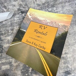 May include: A rectangular book cover featuring a scenic mountain landscape and a road with yellow lines. A central yellow box contains the black text: RV Rentals, a vacationer's guide, Dave & Kay Corby, with a decorative line element included.