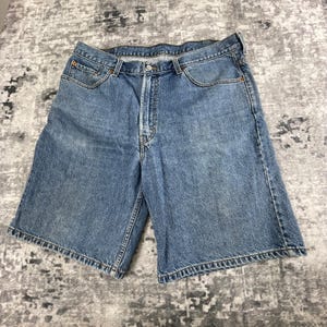 May include: Blue denim shorts with a classic five-pocket design. The shorts have a button and zipper closure, belt loops, and a faded wash. The shorts are made of a durable denim material.