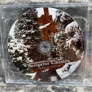 May include: A circular compact disc in a clear plastic case featuring a winter scene with snow-covered evergreen trees and a stone building. The text Navigator Classics Audios & Outlines is printed in white at the bottom center of the disc surface.