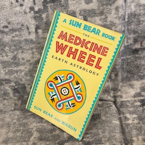 May include: A vintage book titled "The Medicine Wheel Earth Astrology" by Sun Bear and Wabun. The cover is yellow with turquoise and red accents, featuring a circular design with birds and geometric shapes.