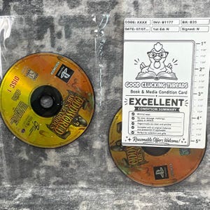 May include: Two circular video game discs for Oddworld: Abe's Exoddus for PlayStation, featuring yellow and orange graphics. A white condition card with a chicken illustration and a 5-inch ruler is placed over one disc, showing the item's status.