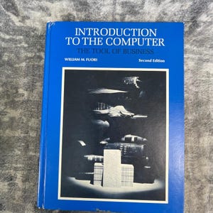 May include: A blue hardcover textbook titled Introduction to the Computer: The Tool of Business by William M. Fuori, Second Edition. The cover features a black and white photograph of stacked books and a punch card centered in a white frame.