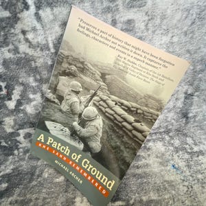 May include: A paperback book titled A Patch of Ground: Khe Sanh Remembered by Michael Archer. The cover features a black and white photograph of soldiers in helmets with rifles positioned behind sandbag fortifications in a trench setting.