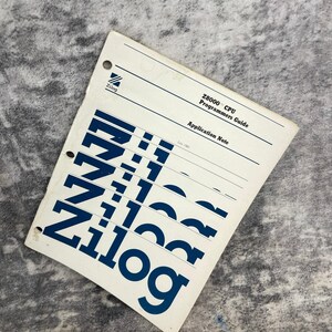May include: A white Zilog Z8000 CPU Programmers Guide application note manual with three punched holes on the left side. The cover features the Zilog logo in the top left corner and the text Zilog repeated in large blue font across the bottom.