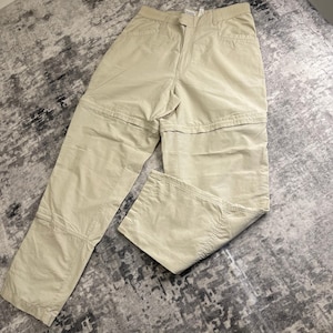 May include: Khaki-colored convertible pants with a zip-off feature, allowing them to transform into shorts. The pants have multiple pockets and a button and zipper closure. The fabric appears to be a lightweight, durable material.