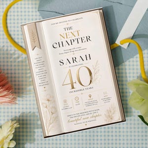 May include: A rectangular invitation card designed to look like an open book. The text reads: The Next Chapter, Sarah is celebrating 40 incredible years. It features gold foil lettering, floral illustrations, and details for date, time, and venue.