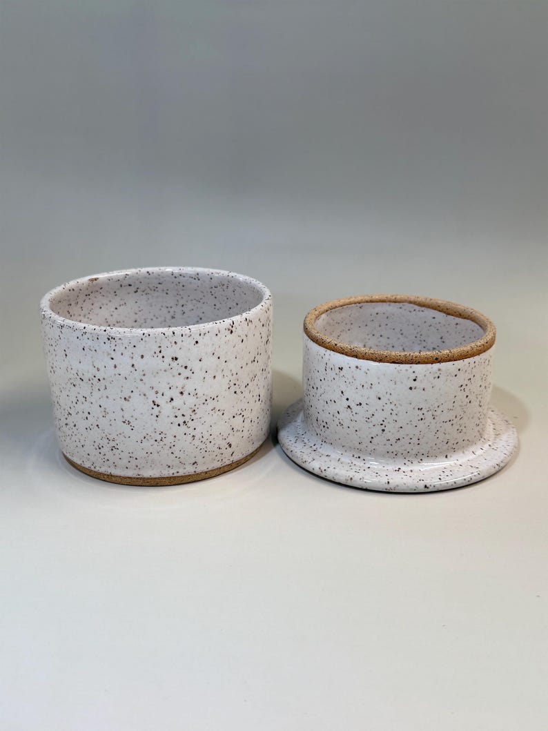 Pu&ograve; includere: Una burriera in ceramica con smalto bianco maculato. Il piatto &egrave; composto da una base cilindrica e un coperchio con la parte superiore arrotondata e un piccolo bordo. Il bordo e la base hanno una finitura naturale non smaltata.
