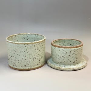Pu&ograve; includere: Un burriera in ceramica in due pezzi. Il piatto &egrave; verde chiaro con macchie marroni e un bordo naturale. Il coperchio &egrave; un cilindro pi&ugrave; piccolo con un motivo maculato abbinato. La base &egrave; un piatto poco profondo.