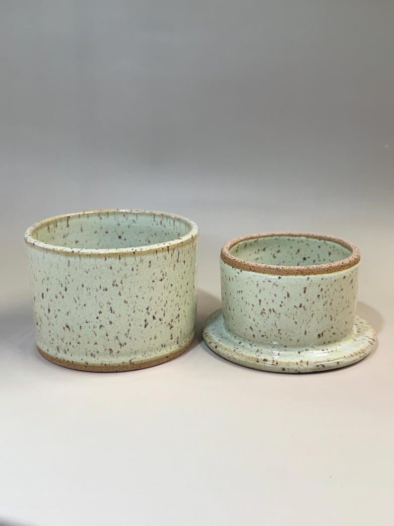 Pu&ograve; includere: Un burriera in ceramica in due pezzi. Il piatto &egrave; verde chiaro con macchie marroni e un bordo naturale. Il coperchio &egrave; un cilindro pi&ugrave; piccolo con un motivo maculato abbinato. La base &egrave; un piatto poco profondo.
