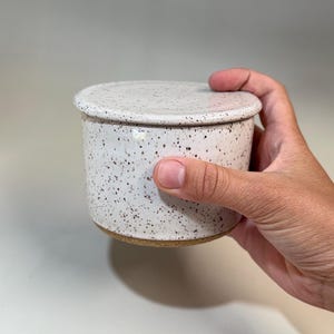 Pu&ograve; includere: Un burriera in ceramica macchiata con coperchio. Il piatto &egrave; cilindrico con un coperchio arrotondato, entrambi di colore bianco crema con macchie marroni. La base del piatto &egrave; di colore argilla naturale non smaltata.