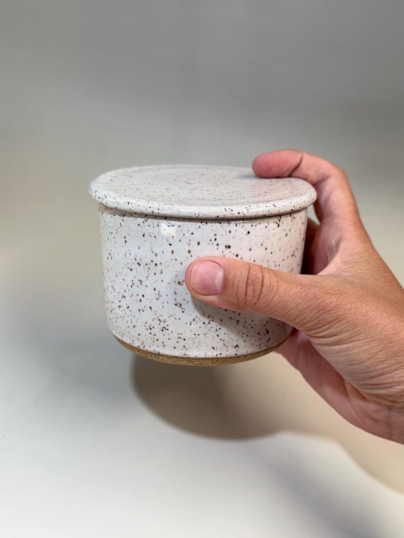 Pu&ograve; includere: Un burriera in ceramica macchiata con coperchio. Il piatto &egrave; cilindrico con un coperchio arrotondato, entrambi di colore bianco crema con macchie marroni. La base del piatto &egrave; di colore argilla naturale non smaltata.