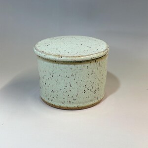 Pu&ograve; includere: Una burriera in ceramica con coperchio. Il piatto cilindrico ha una glassa maculata verde chiaro e un bordo marrone pi&ugrave; scuro. Il coperchio rotondo si adatta perfettamente. Un articolo di ceramica fatto a mano.