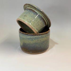 Pu&ograve; includere: Un burriera in ceramica fatta a mano con coperchio. Il piatto e il coperchio sono smaltati in tonalit&agrave; di verde e blu, con una texture maculata. Il bordo del piatto e del coperchio &egrave; marrone scuro. La burriera &egrave; progettata per contenere una confezione di burro standard.
