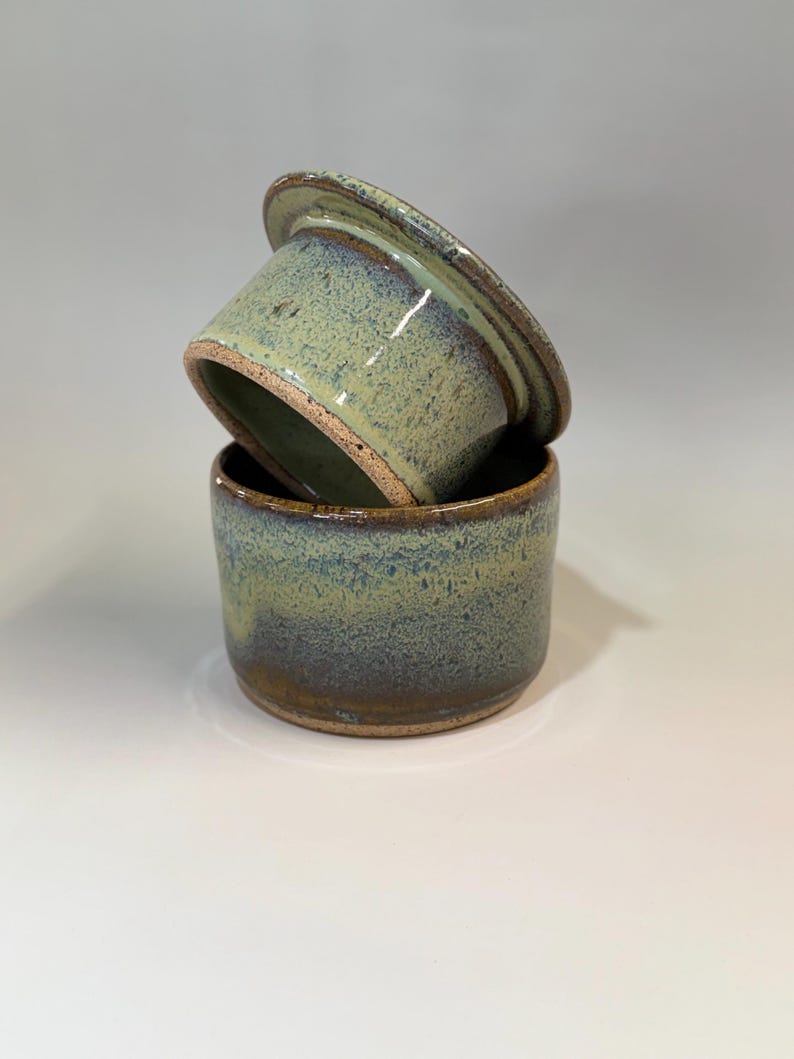 Pu&ograve; includere: Un burriera in ceramica fatta a mano con coperchio. Il piatto e il coperchio sono smaltati in tonalit&agrave; di verde e blu, con una texture maculata. Il bordo del piatto e del coperchio &egrave; marrone scuro. La burriera &egrave; progettata per contenere una confezione di burro standard.