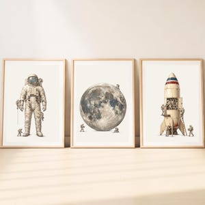 May include: A set of three framed art prints featuring space themes. The first shows a large astronaut with smaller figures. The second depicts a detailed moon with tiny astronauts on its surface. The third shows a rocket ship with astronauts.