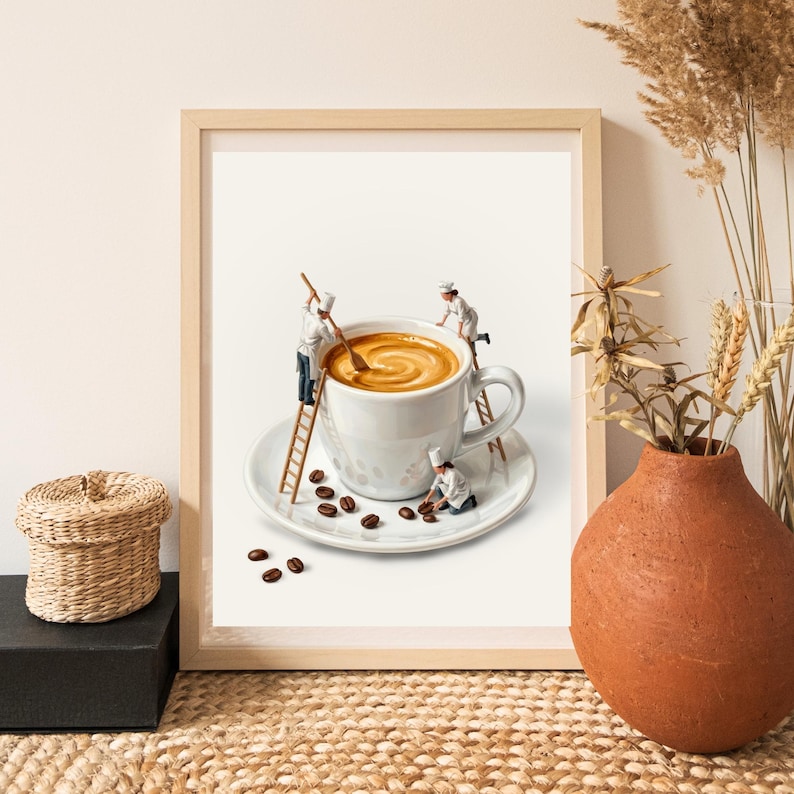 May include: A framed print depicts a whimsical scene of miniature chefs preparing coffee in a large white mug. The coffee cup sits on a saucer with scattered coffee beans. The chefs use a ladder and spoons to stir the coffee.