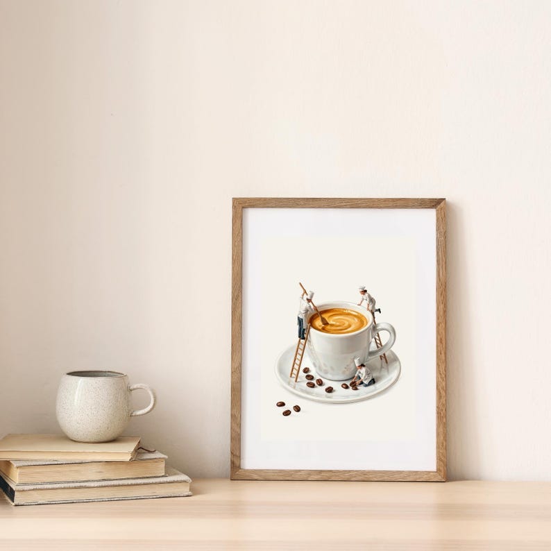 May include: A framed art print featuring a white coffee cup on a saucer with miniature figures of chefs using ladders to stir the coffee and arrange coffee beans. The scene is set against a plain background, capturing a whimsical culinary concept.