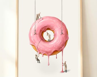 Puede incluir: Impresión artística enmarcada que representa un gran donut glaseado rosa con chefs en miniatura. El donut tiene una base marrón dorada y glaseado rosa goteando. Los chefs, con uniformes blancos, están suspendidos por cuerdas.