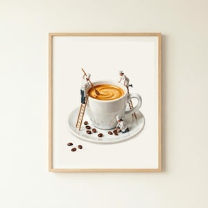 May include: A framed art print featuring a white ceramic coffee cup filled with latte on a matching saucer. Three miniature figures dressed in white chef uniforms are interacting with the cup, using wooden ladders and stirring the coffee.