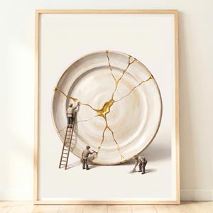 May include: A framed wall art print featuring a large, off-white ceramic plate with golden cracks. Three miniature figures in work clothes are repairing the plate, with one on a wooden ladder and two on the ground using tools.