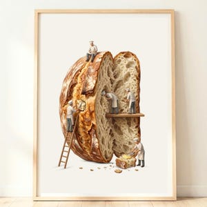 Op de afbeelding: Een ingelijste kunstdruk met een grote, doorgesneden zuurdesembrood. Miniatuurfiguurtjes van bakkers in witte uniformen werken aan het brood, met één op een ladder, twee in de kruim en één die een stukje brood met boter besmeert.