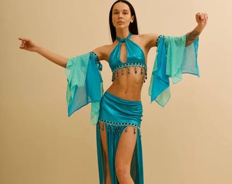 May include: A turquoise belly dance costume with a halter top, flowing sleeves, and a high-slit skirt. The outfit is adorned with beaded embellishments and is designed for dance performances. The costume is made of a shiny, reflective fabric.
