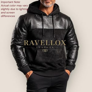 Könnte beinhalten: Schwarzer Leder-Hoodie mit Krokodil-Textur-Einsätzen und Ärmeln. Der Hoodie hat eine Kängurutasche und eine Kapuze mit Kordelzug. Der Markenname "RAVELLOX LEATHER" ist in Gold. Die tatsächliche Farbe kann leicht abweichen.