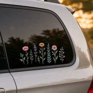Puede incluir: Un adhesivo de vinilo aplicado en la ventana de un coche que muestra una fila de flores silvestres coloridas. El diseño incluye ilustraciones botánicas en rosa, morado, naranja y verde de varios tallos, hojas y flores en línea horizontal.