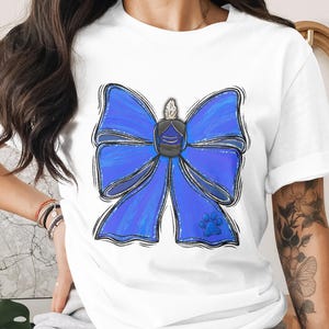Könnte beinhalten: Weißes T-Shirt mit einer großen, stilisierten blauen Schleife mit schwarzen Umrissen. Die Schleife hat ein zentrales Emblem und einen Pfotenabdruck. Das Design ist eine digitale Illustration, für Kleidung.